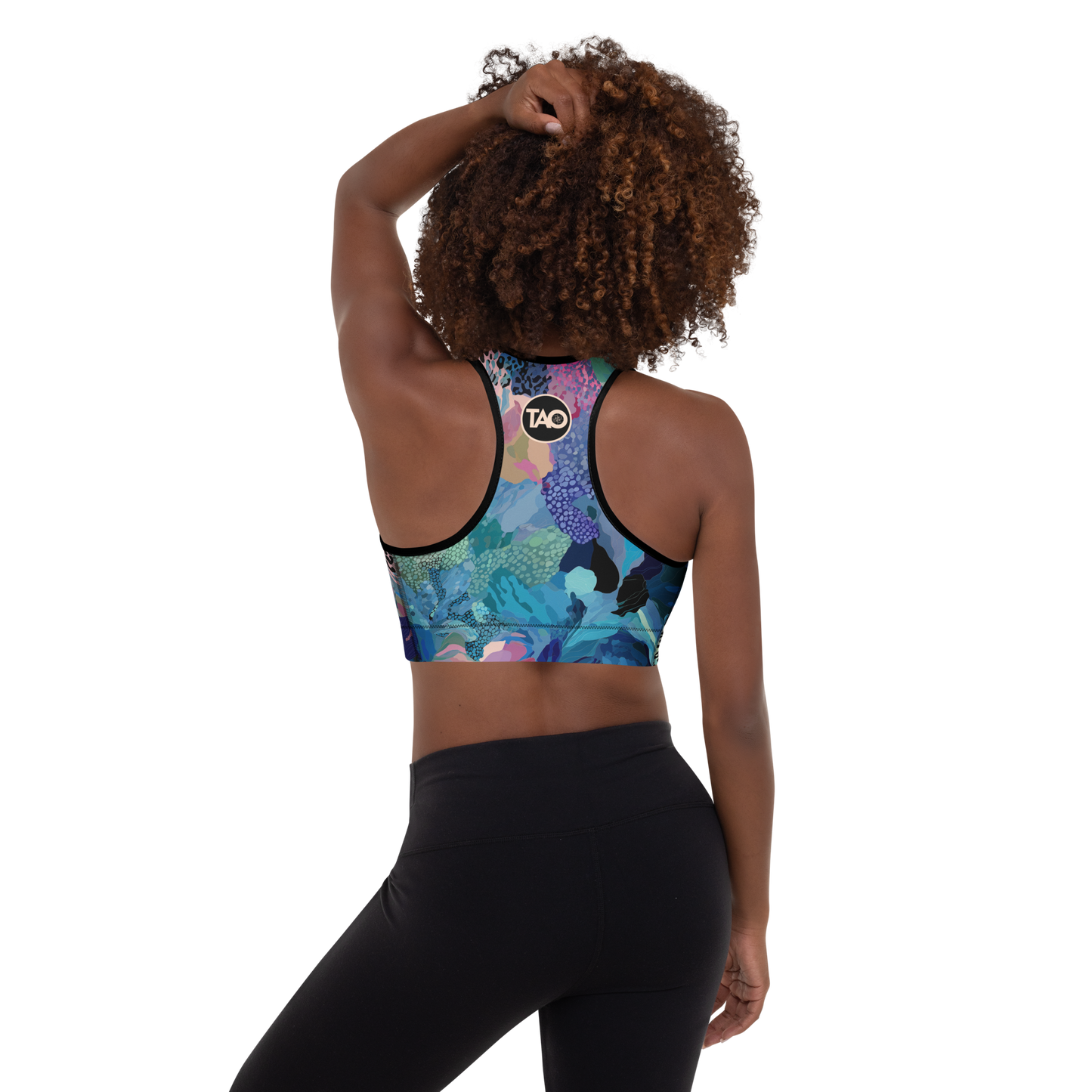 Woman wearing a blue camo-print sports bra with scoop neckline, racerback, and wide underband — made from moisture-wicking, four-way stretch fabric with removable padding for active support and bold style.