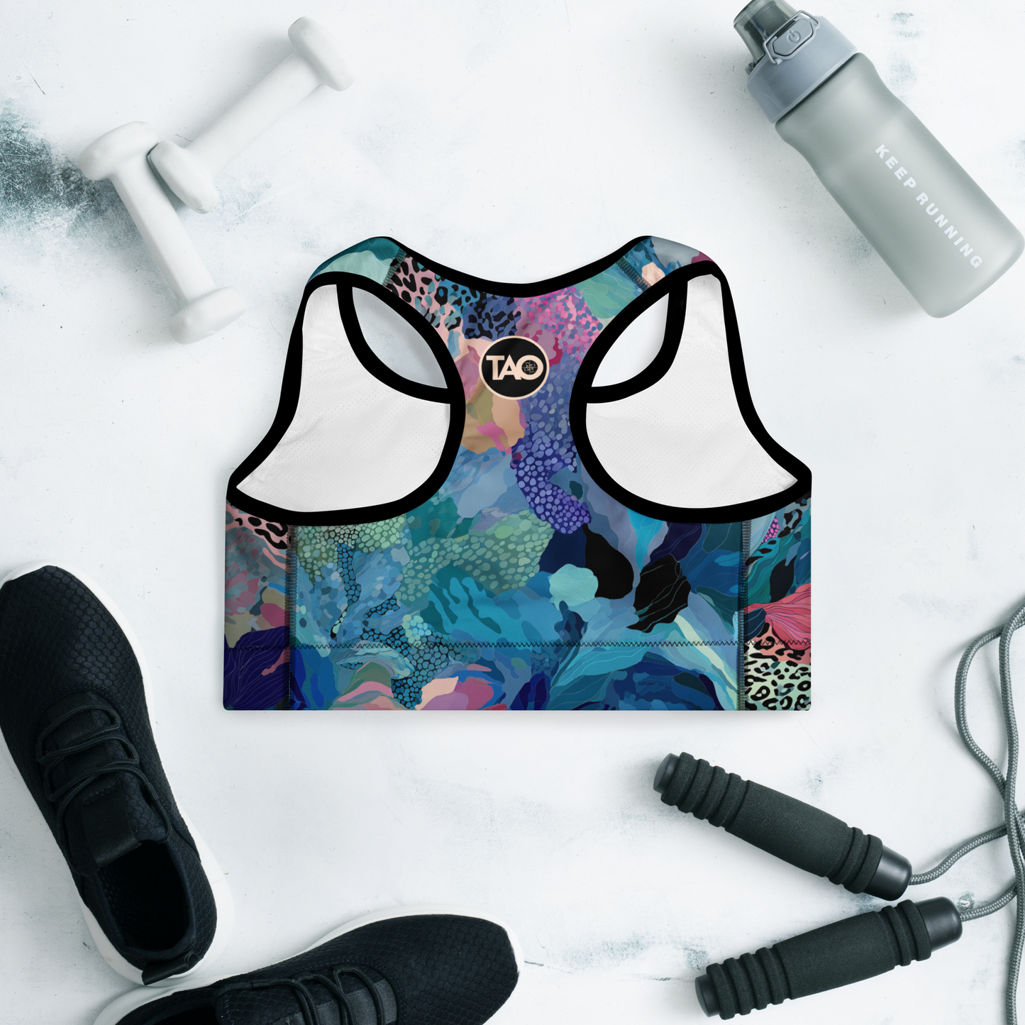 Woman wearing a blue camo-print sports bra with scoop neckline, racerback, and wide underband — made from moisture-wicking, four-way stretch fabric with removable padding for active support and bold style.