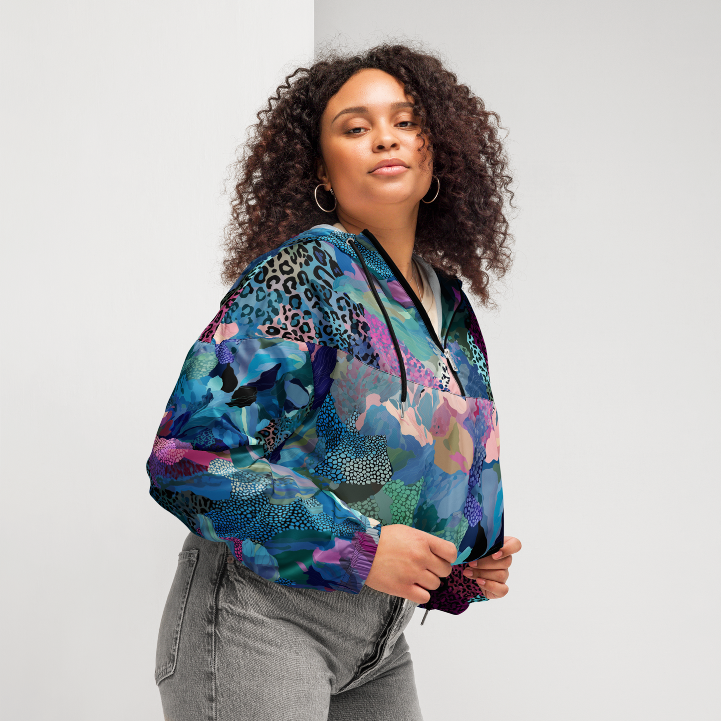A woman wearing Cropped windbreaker featuring a bold blue camo print with adjustable hood and waist drawcords, breathable mesh lining, and side-slit pockets — designed for lightweight protection and standout style.