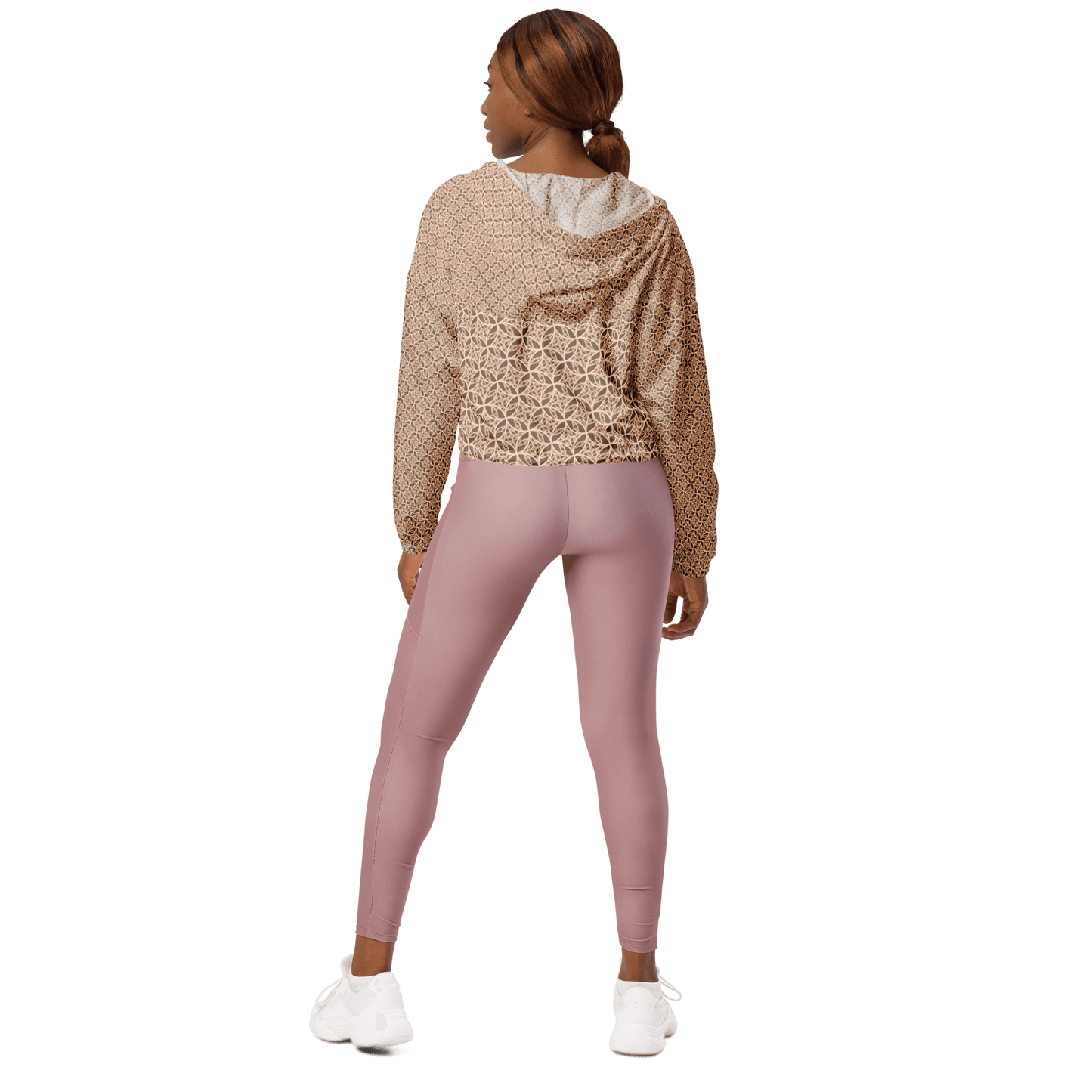 Woman wearing a lightweight beige cropped windbreaker with monogram Fibonacci pattern, featuring adjustable drawcords, side-slit pockets, and mesh lining — a waterproof, sacred-geometry inspired layer for mindful movement and conscious living.