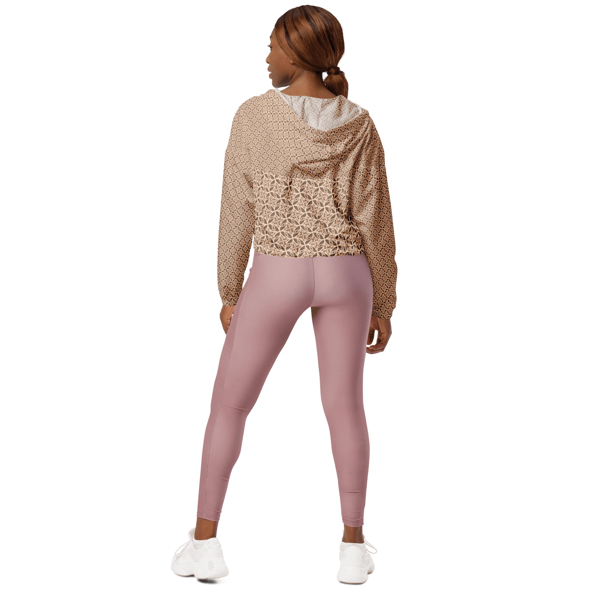 Woman wearing a lightweight beige cropped windbreaker with monogram Fibonacci pattern, featuring adjustable drawcords, side-slit pockets, and mesh lining — a waterproof, sacred-geometry inspired layer for mindful movement and conscious living.