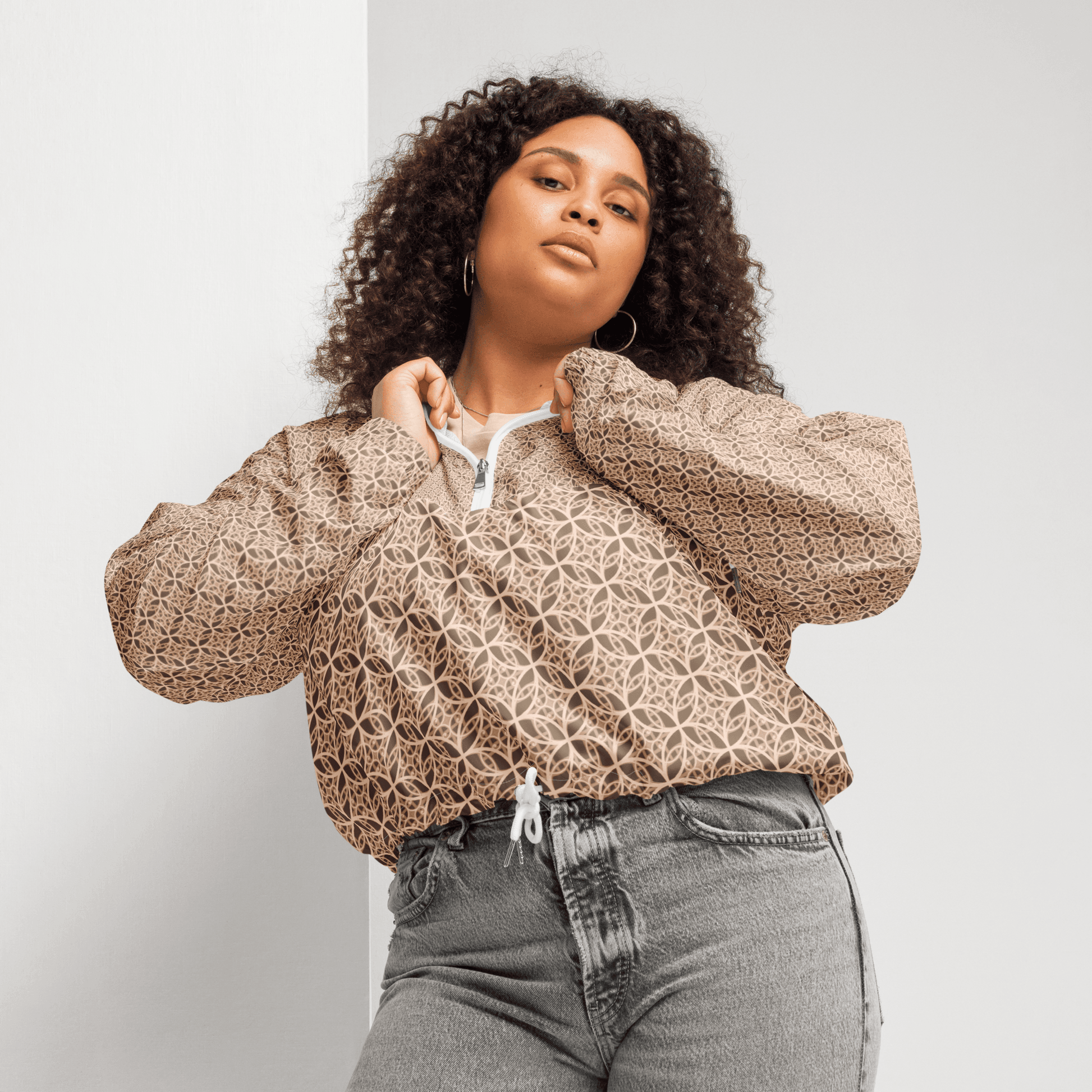 Woman wearing a lightweight beige cropped windbreaker with monogram Fibonacci pattern, featuring adjustable drawcords, side-slit pockets, and mesh lining — a waterproof, sacred-geometry inspired layer for mindful movement and conscious living.
